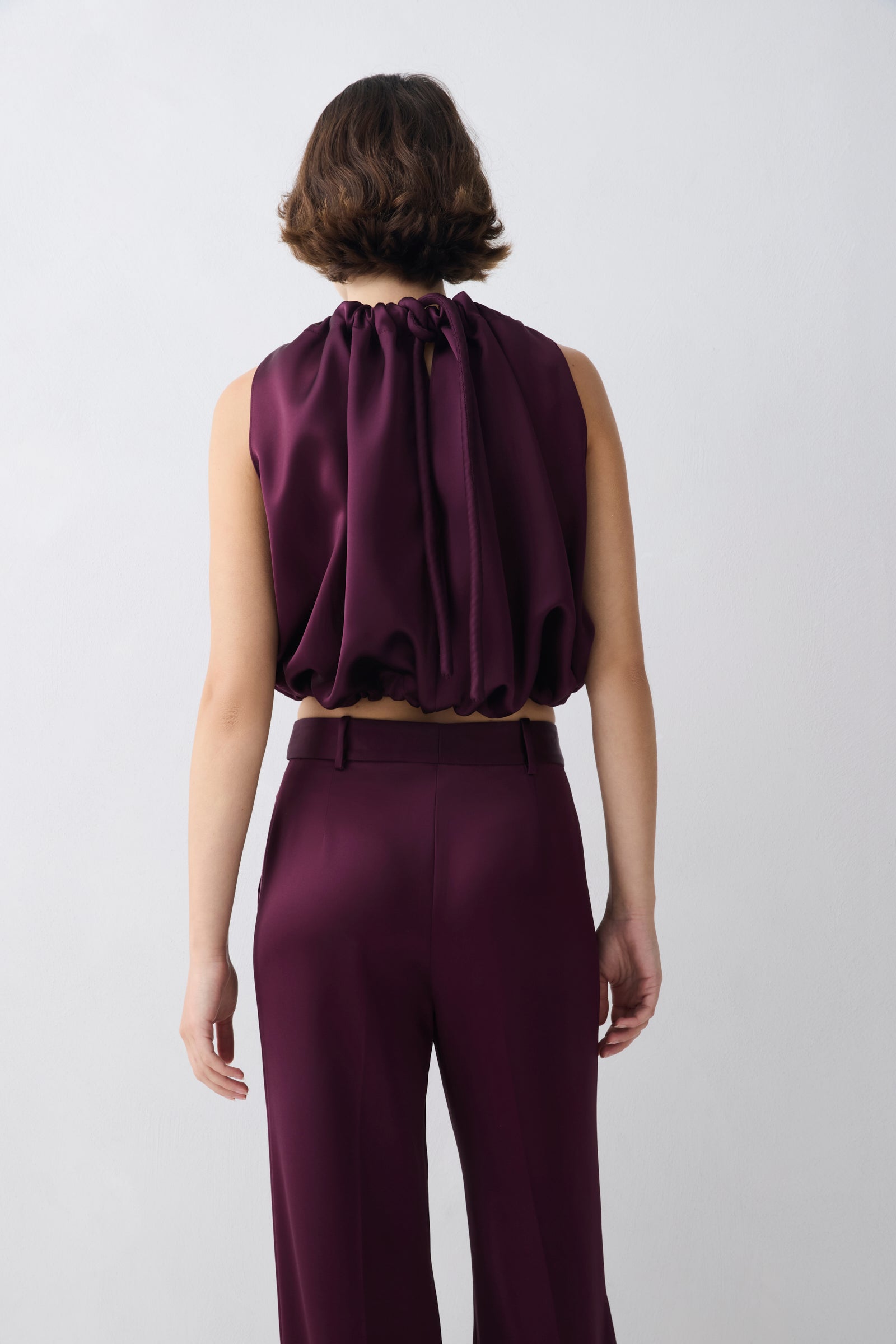 Person wearing a purple outfit with a halter neck top and wide-leg pants on a white background