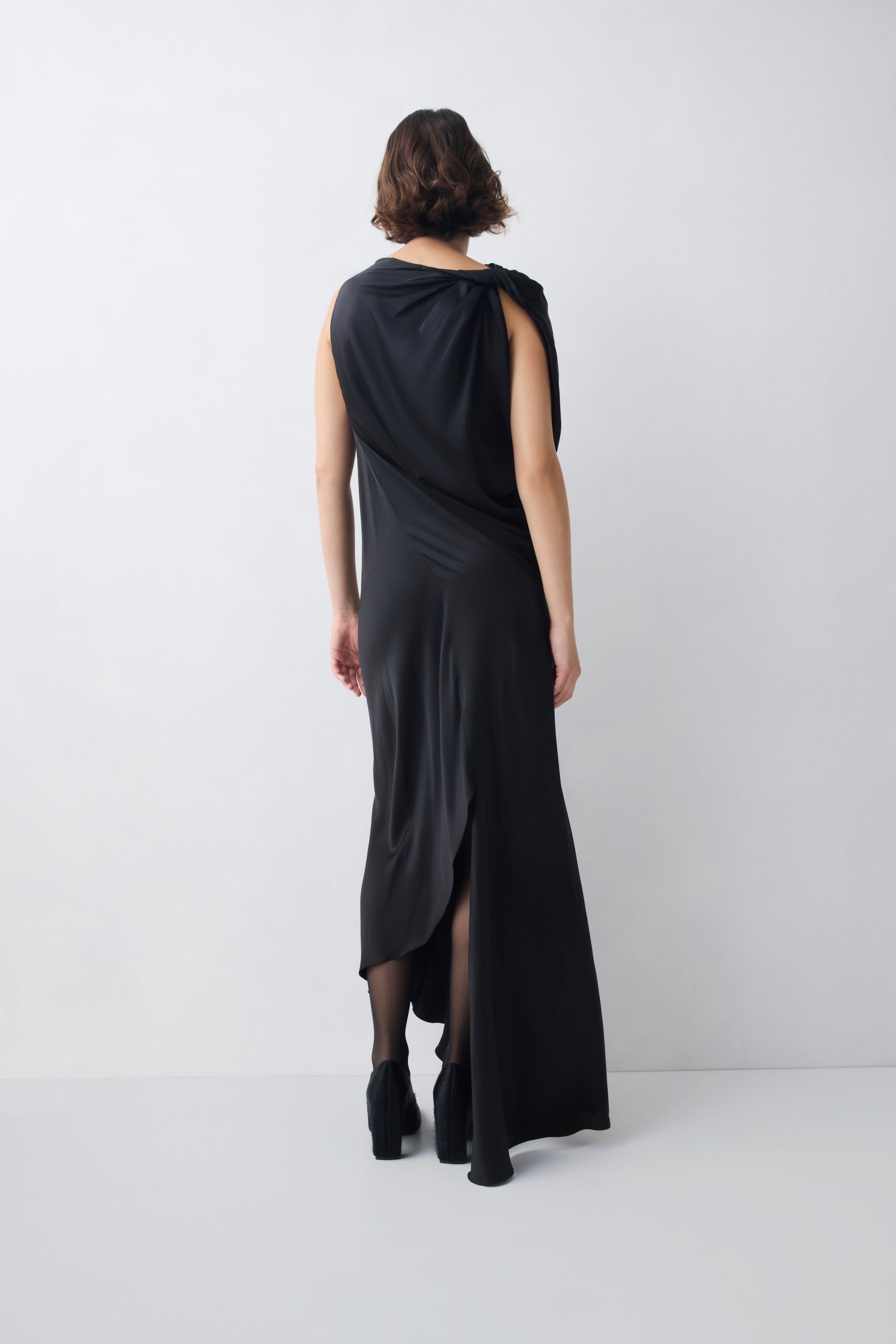 Woman wearing a black sleeveless dress with a slit on a white background
