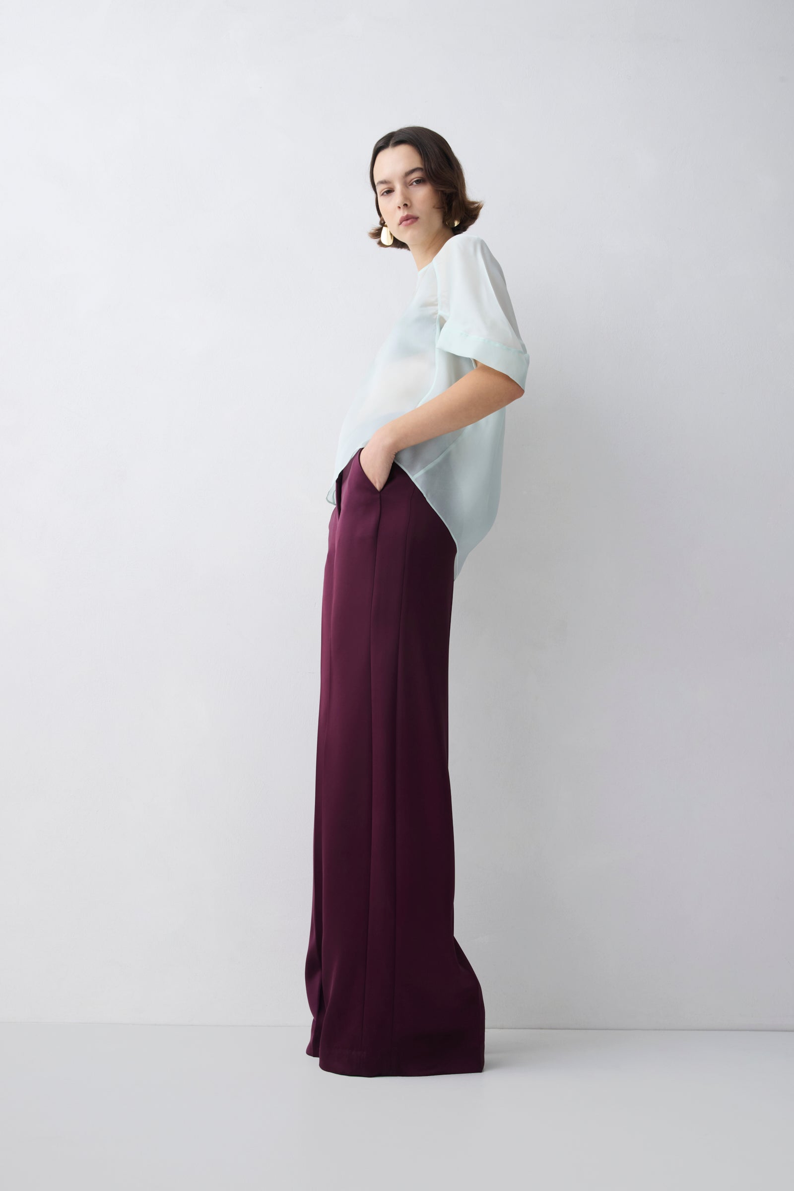Woman wearing a white top and purple pants against a white background