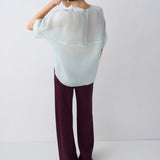 Person wearing a white blouse and dark pants against a white background