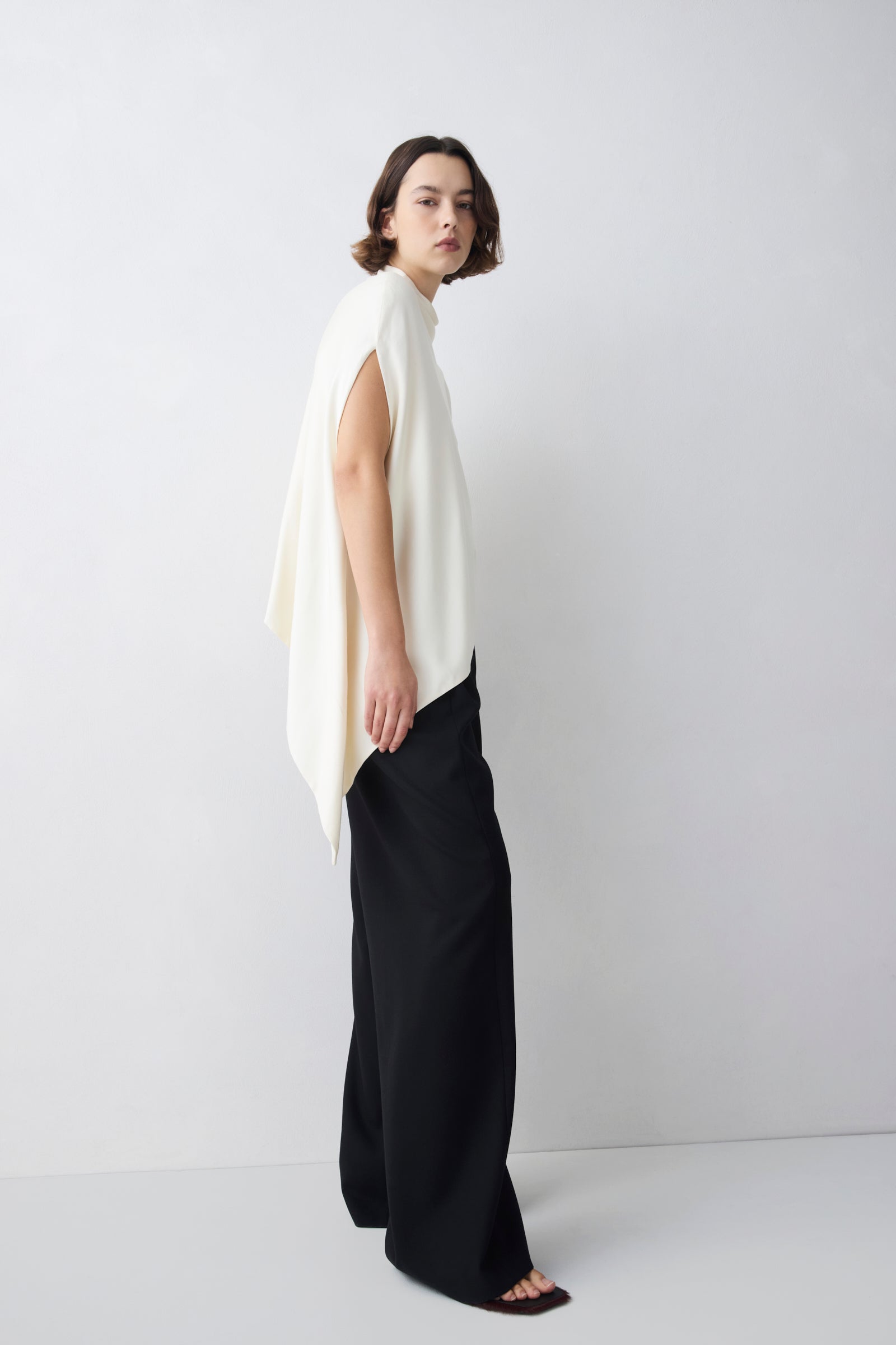 Woman wearing a white sleeveless top and black pants on a white background