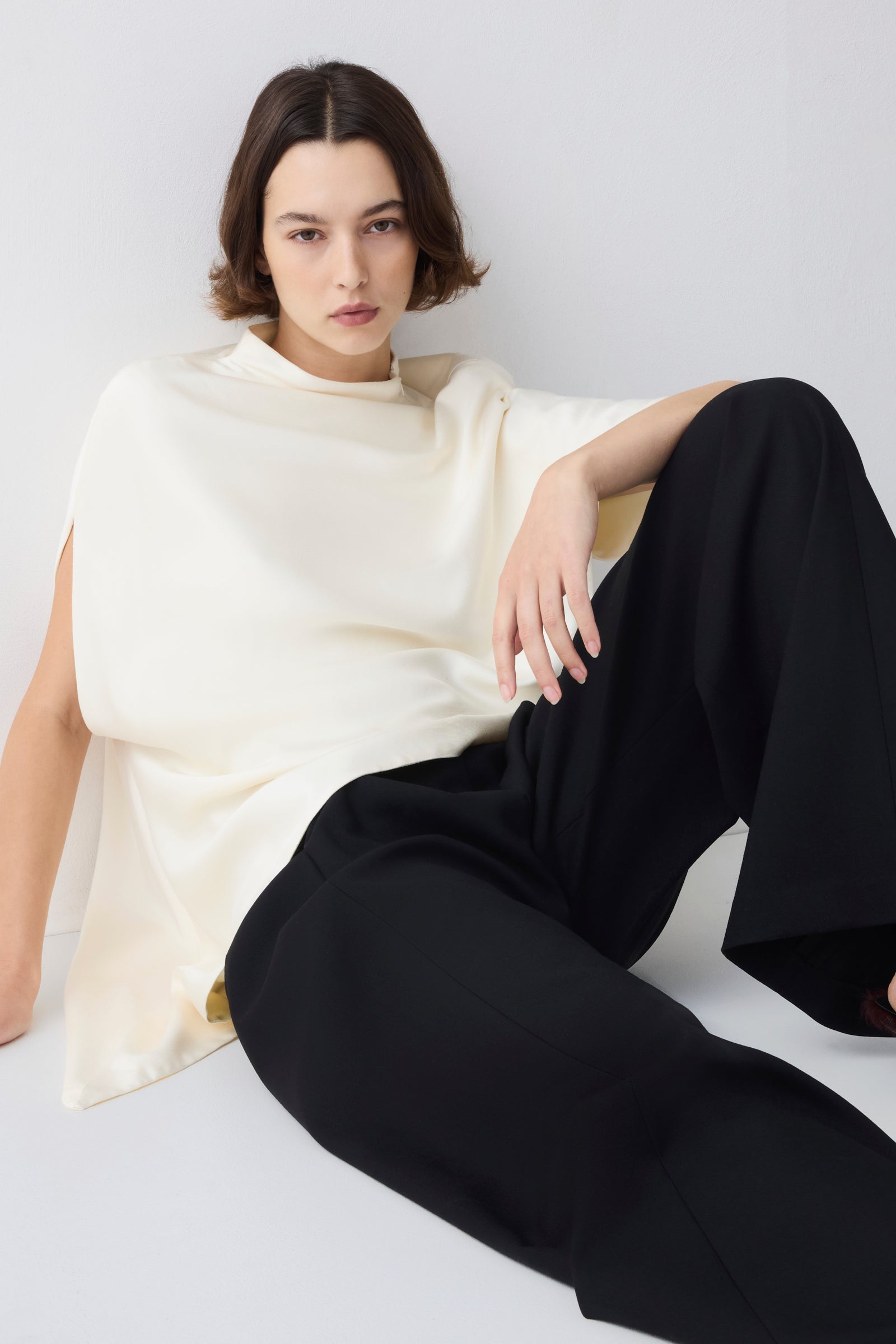Person wearing a white top and black pants sitting on a white surface.