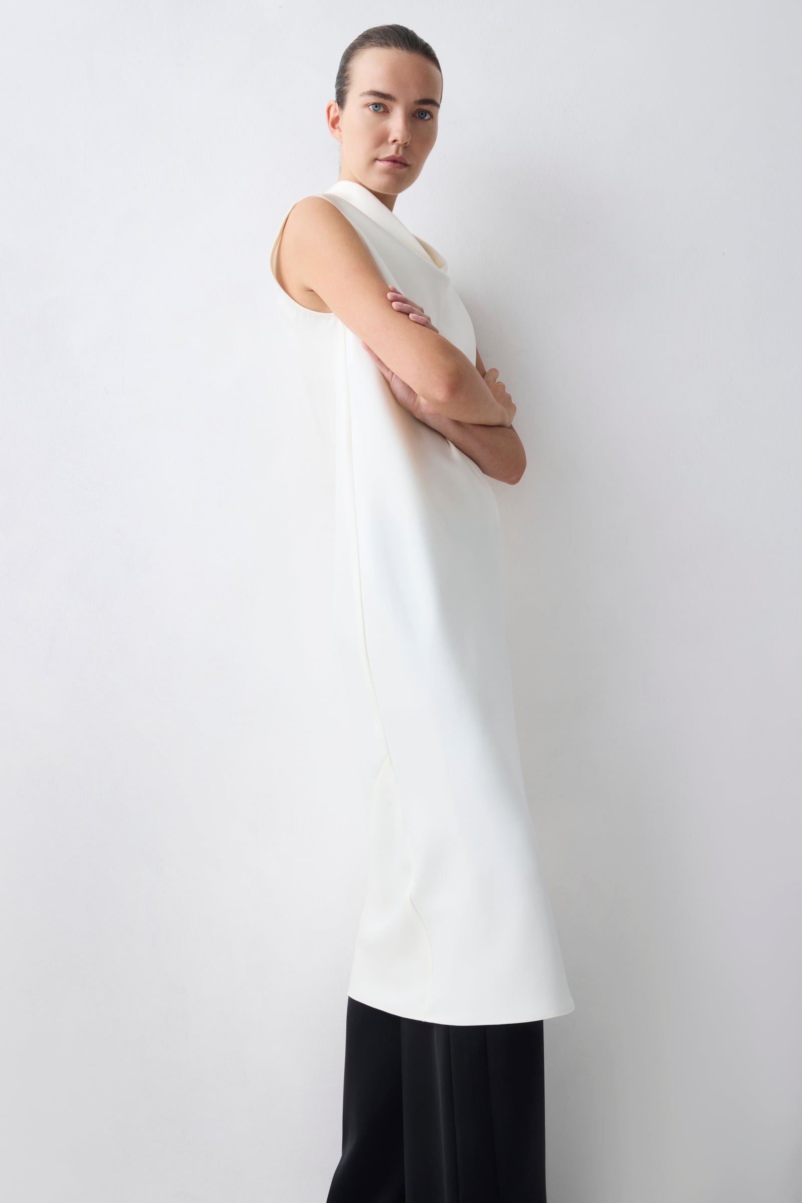 Person wearing a white sleeveless top and black pants against a plain background