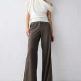 Woman wearing a white top and brown pants against a plain background