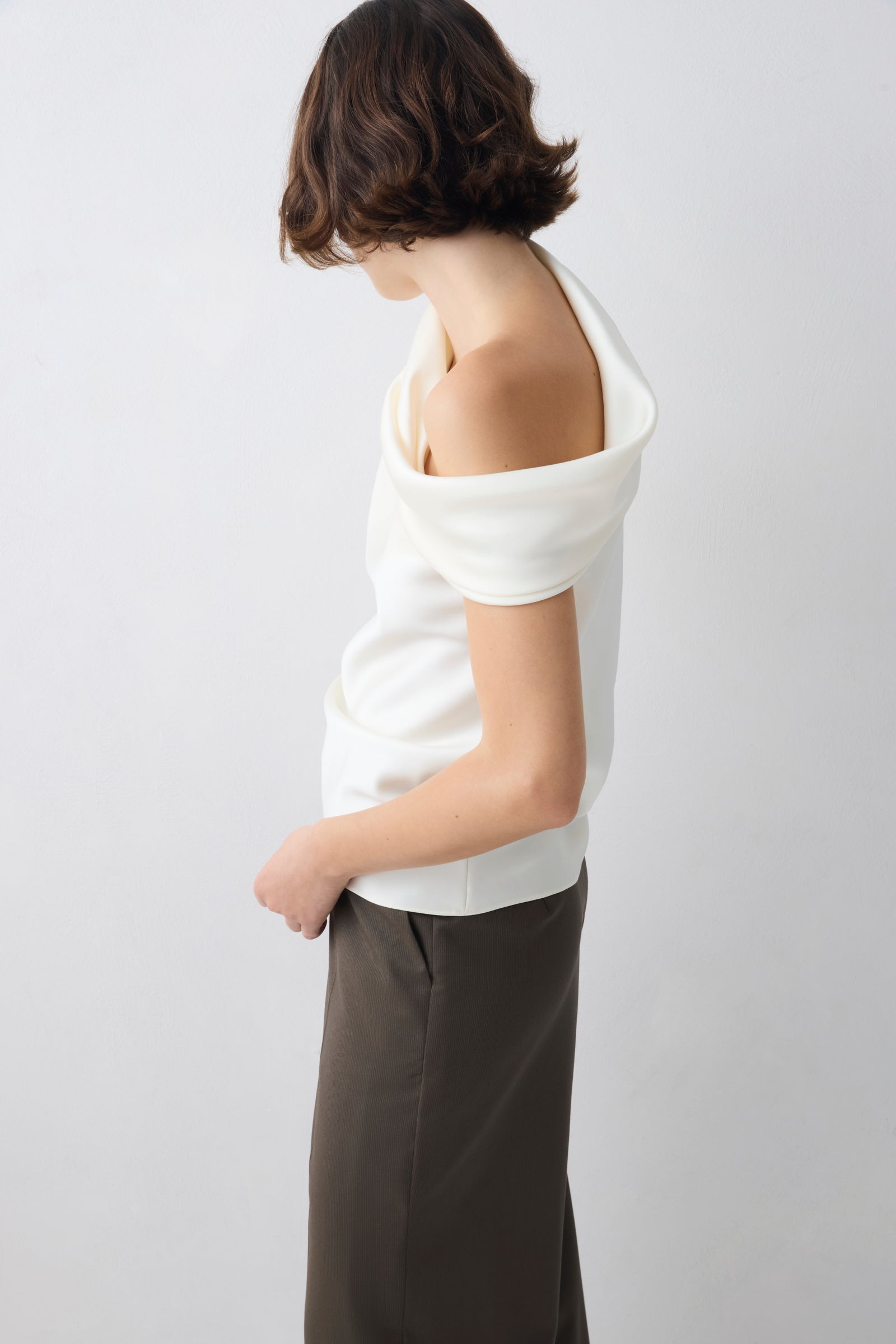 Person wearing a white off-shoulder top and dark pants on a light gray background