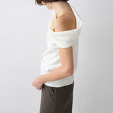 Person wearing a white off-shoulder top and dark pants on a light gray background