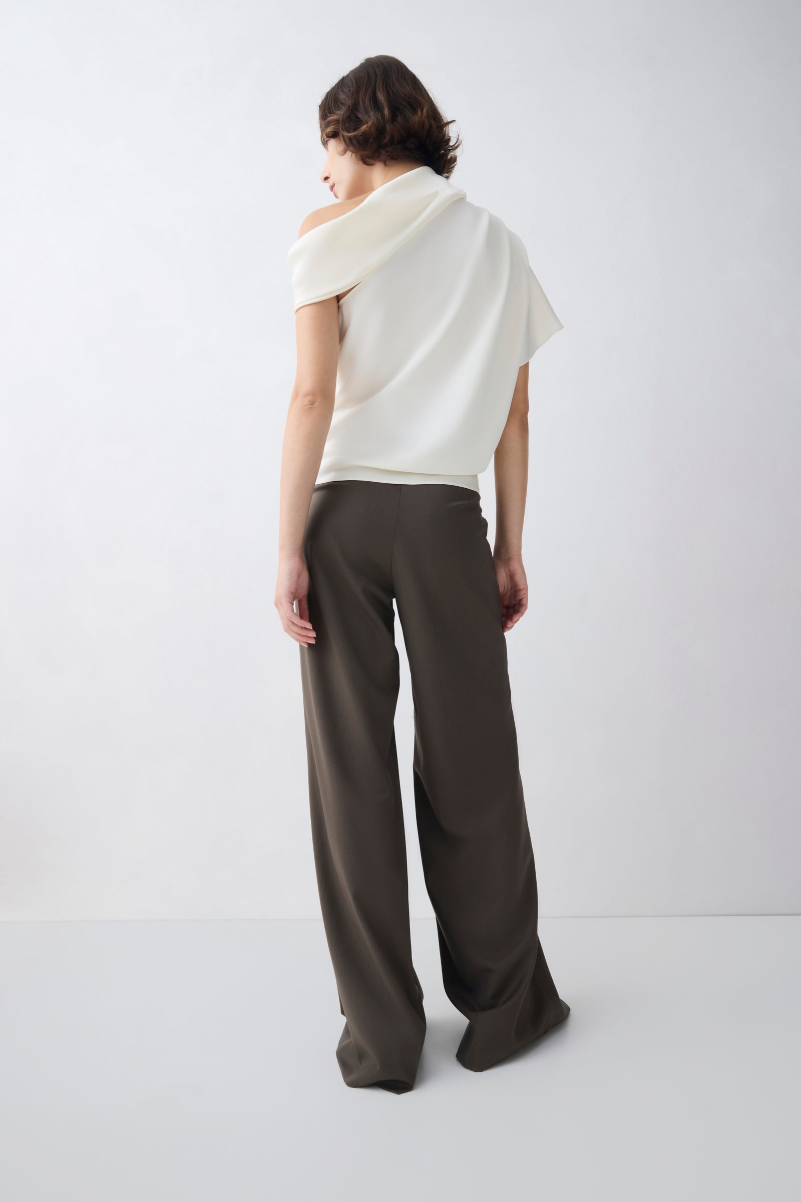 Person wearing a white off-shoulder top and dark pants on a white background