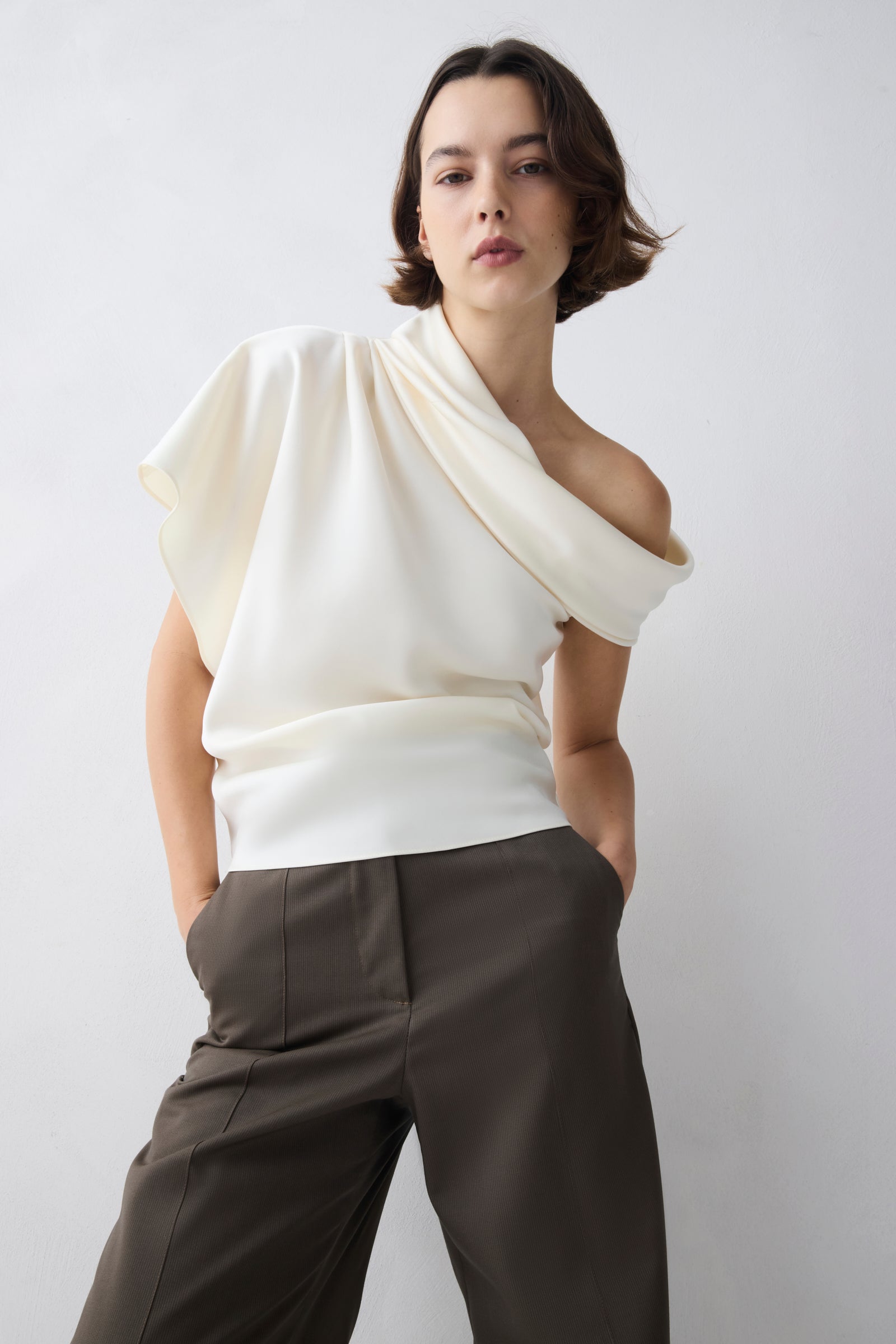 Person wearing a white off-shoulder top and brown pants against a plain background