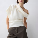 Person wearing a white off-shoulder top and brown pants against a plain background