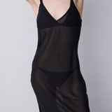 A model wearing a sheer black slip dress over black lingerie, photographed against a plain light gray studio background.