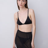 A model wearing a black lingerie set consisting of a black satin triangle bra and matching sheer black mesh pants, standing against a light gray studio background.