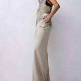 A model wearing a beige satin-like draped top and matching wide-leg trousers, posing against a light gray studio background.