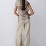 A model shown from the back wearing a shimmering metallic taupe top and matching wide-leg trousers against a light gray studio background.