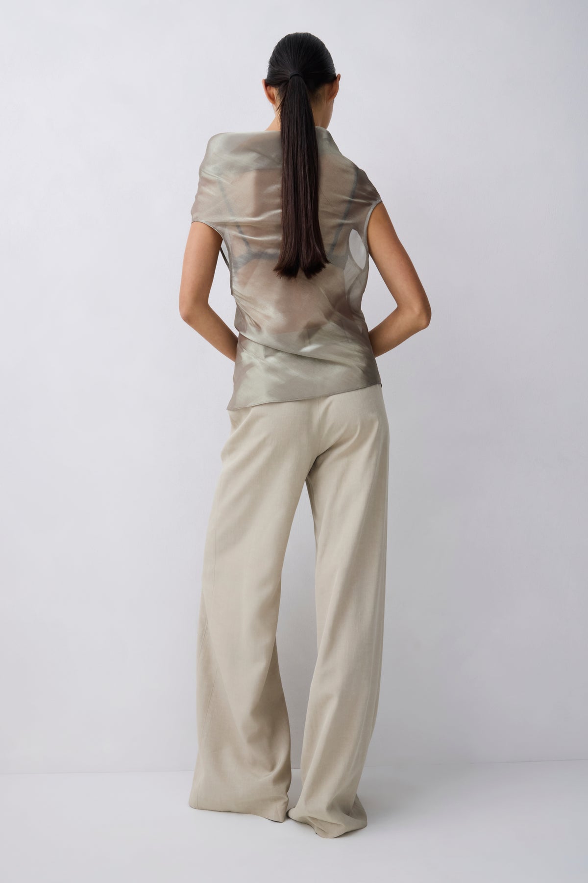 A model shown from the back wearing a shimmering metallic taupe top and matching wide-leg trousers against a light gray studio background.