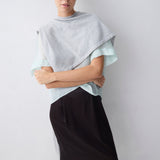 Woman wearing a light gray top and black skirt against a white background