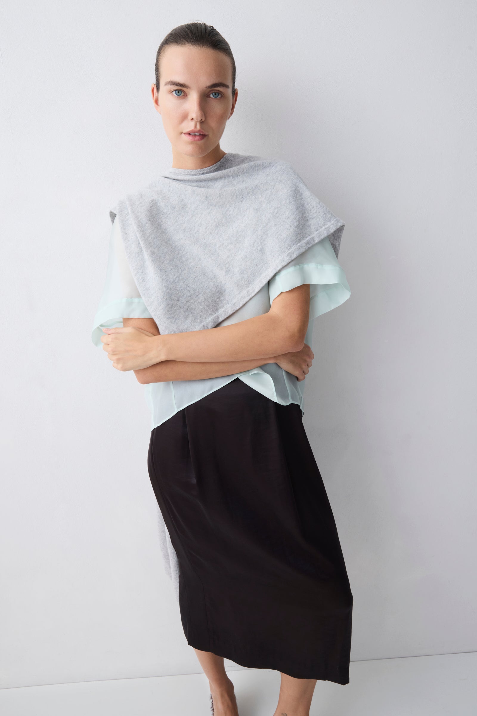 Woman wearing a light gray top and black skirt against a white background