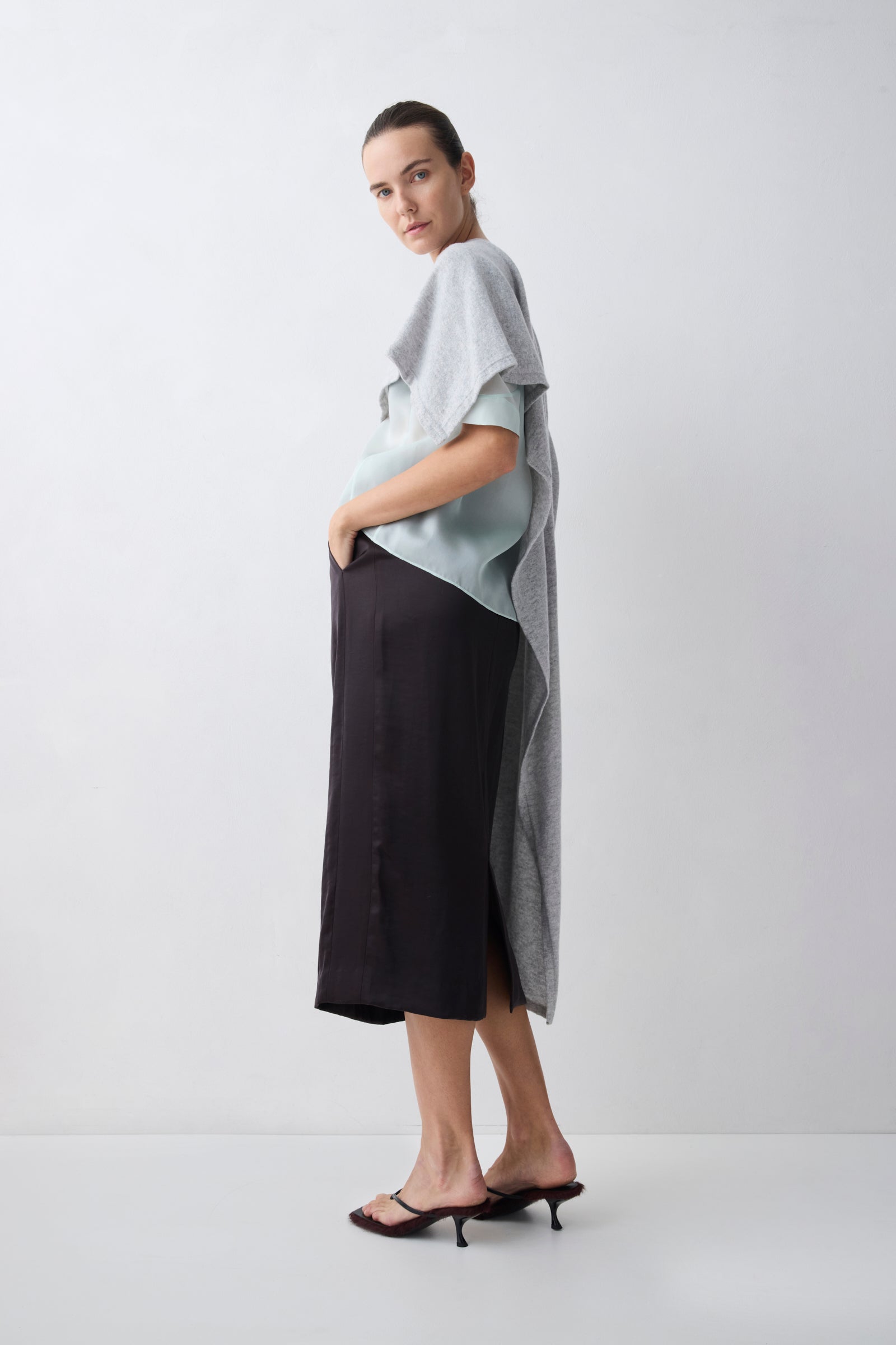 Woman wearing a light gray top and black skirt on a white background