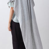 Person wearing a gray poncho over a light blue top and black pants on a white background