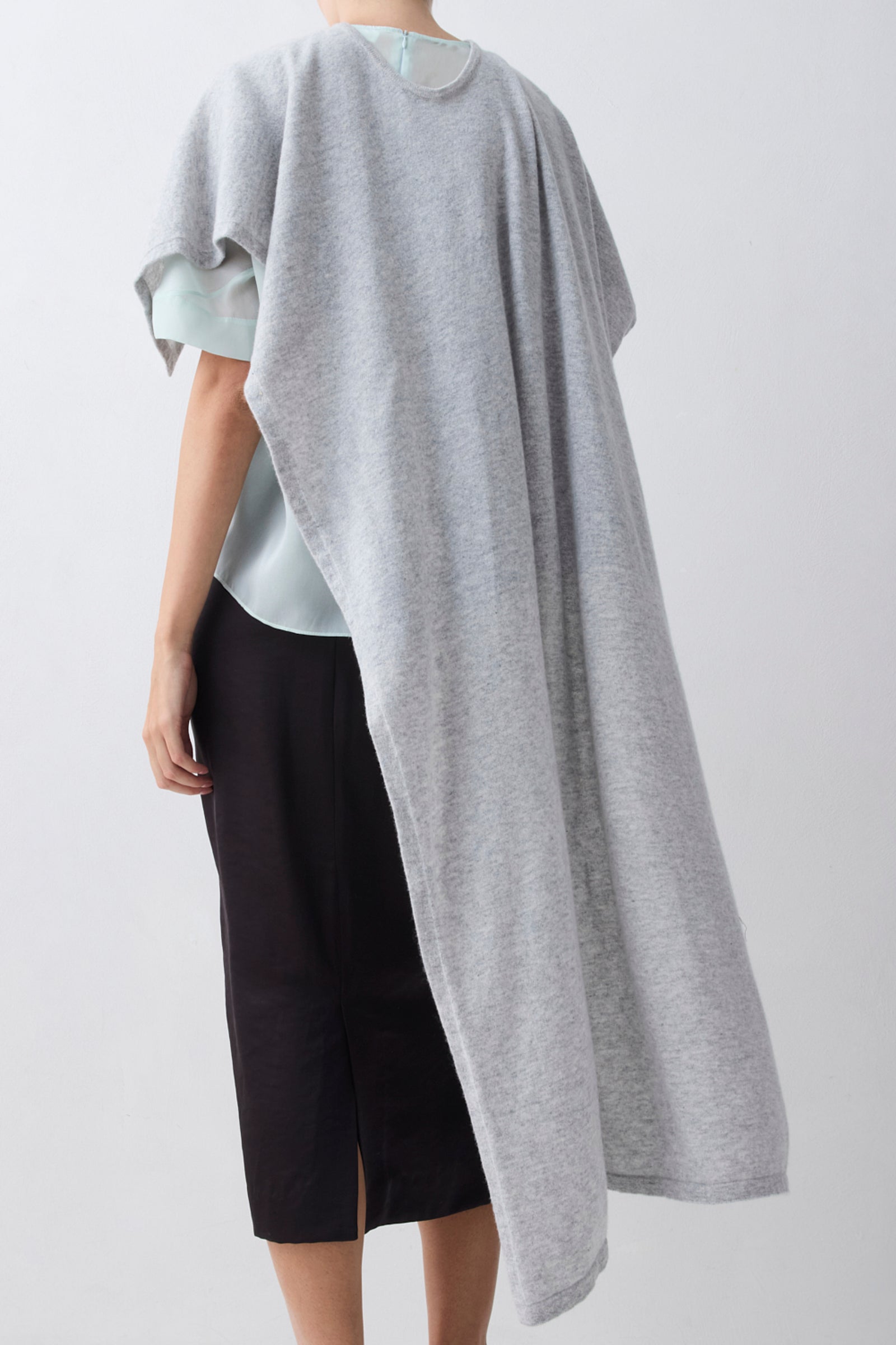 Person wearing a gray poncho over a light blue top and black pants on a white background