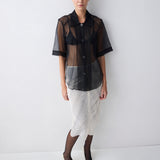 Person wearing a black sheer blouse over a patterned skirt on a white background