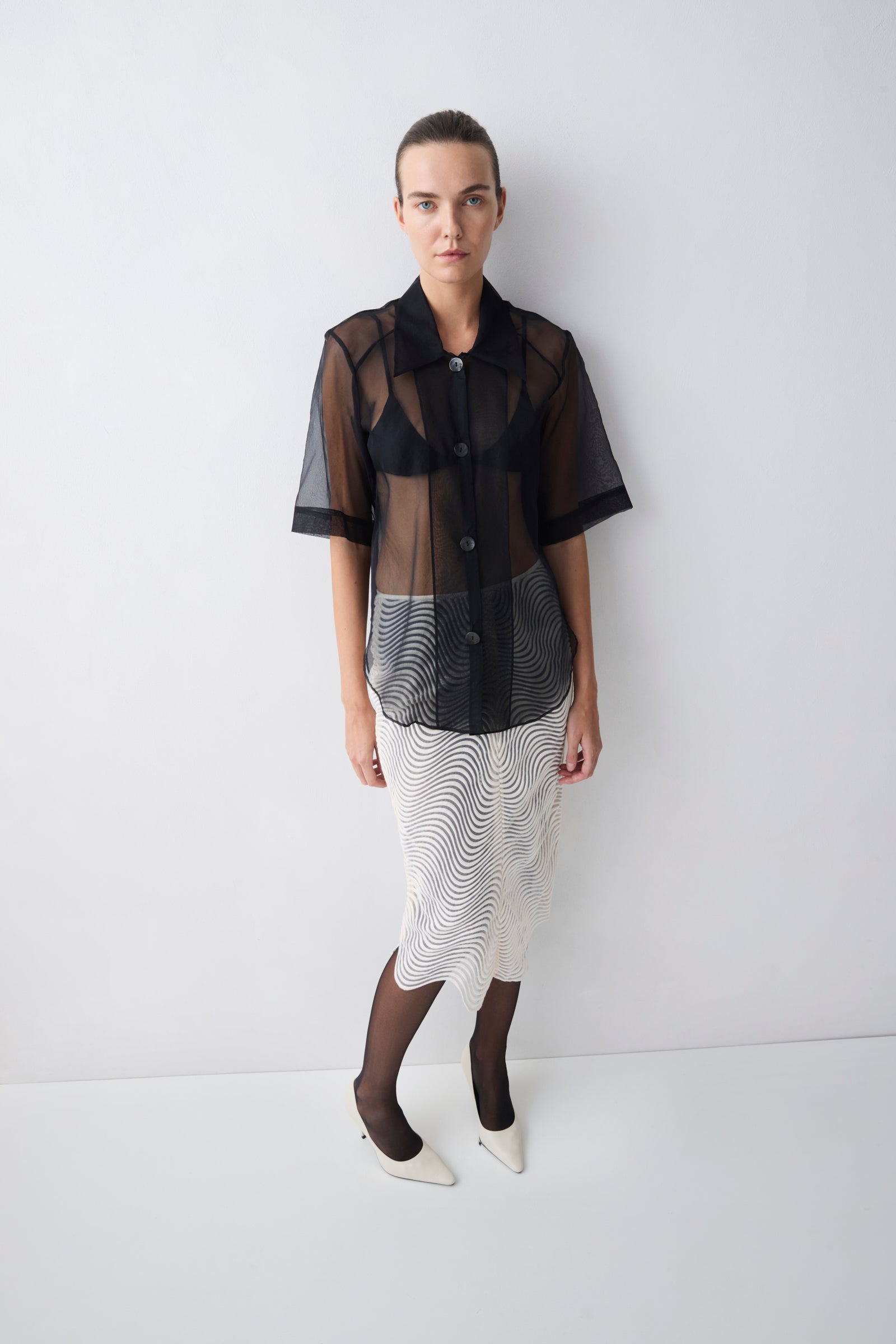 Person wearing a black sheer blouse over a patterned skirt on a white background