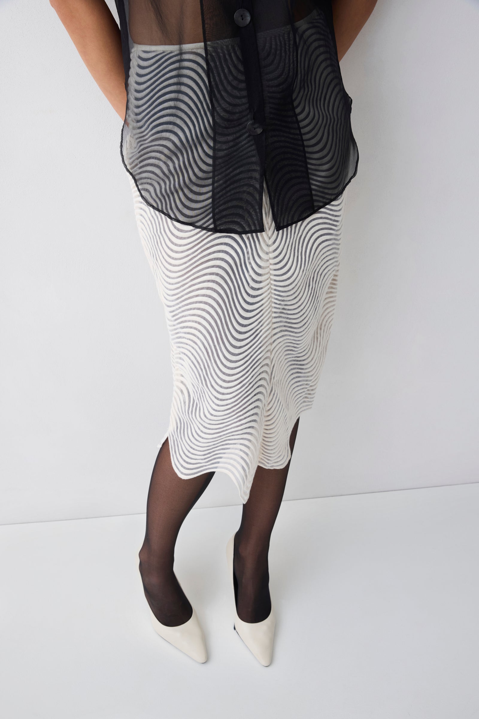 Person wearing a black and white patterned dress with sheer black stockings on a white background