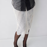 Person wearing a black and white patterned dress with sheer black stockings on a white background