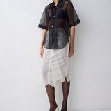 Woman wearing a black sheer blouse over a patterned skirt on a white background