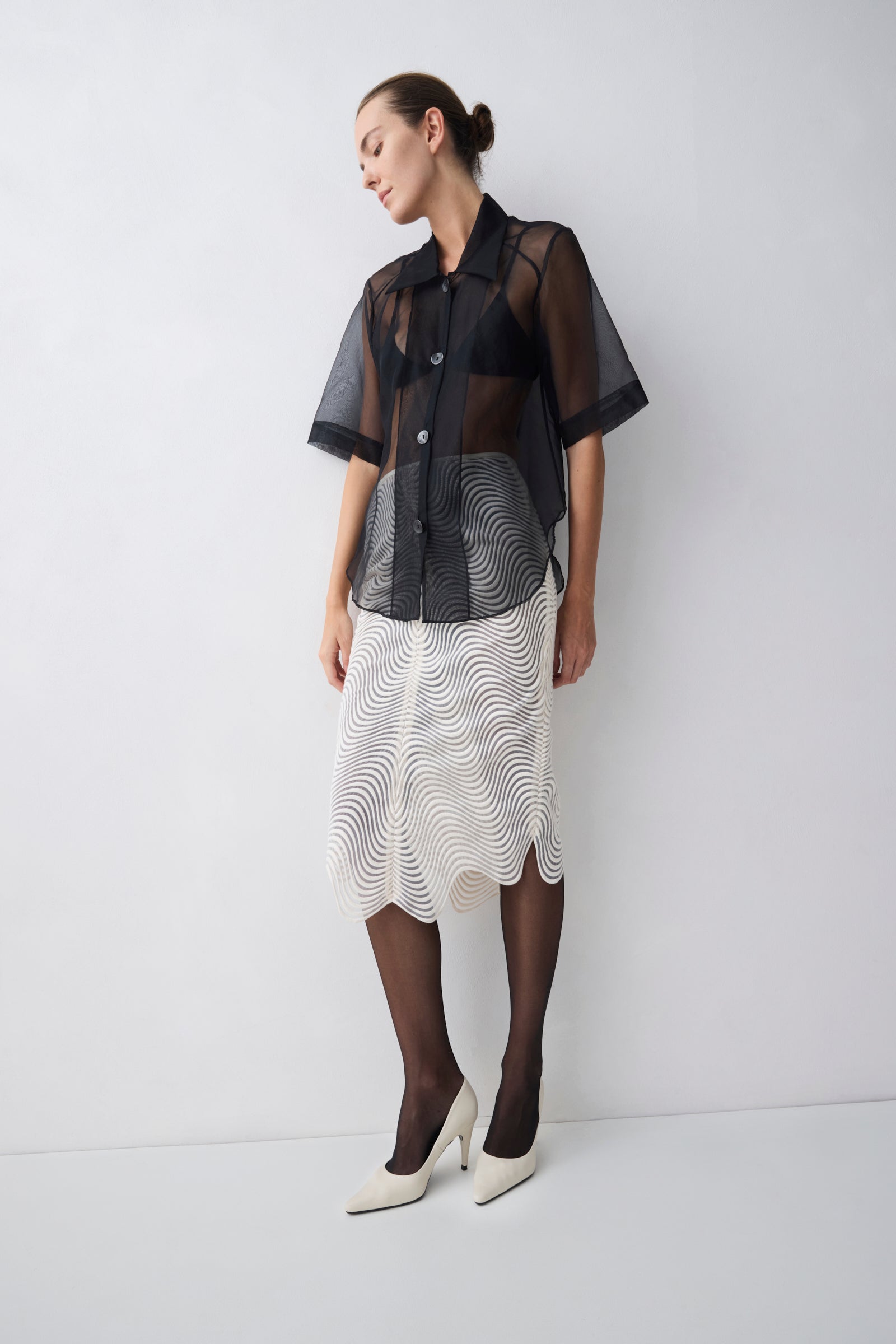 Woman wearing a black sheer blouse over a patterned skirt on a white background