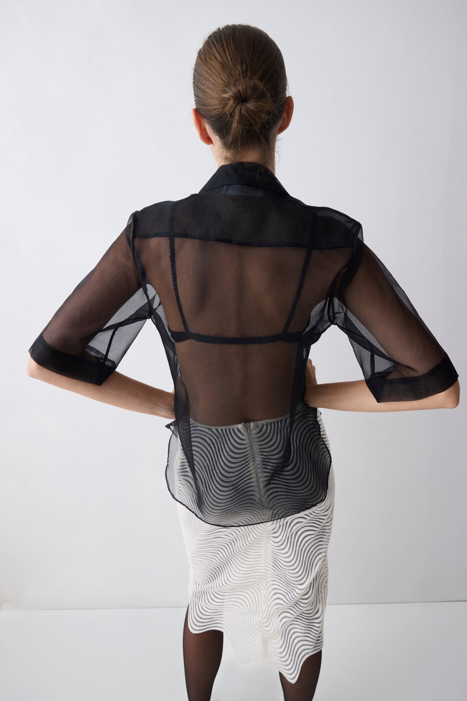Woman wearing a black sheer top over a patterned dress on a white background