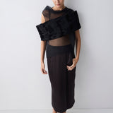 Woman wearing a black outfit with sheer top against a white background
