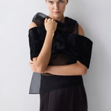 Woman wearing a black outfit with sheer sleeves against a white background