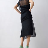 Woman wearing a black dress with sheer sleeves against a white background