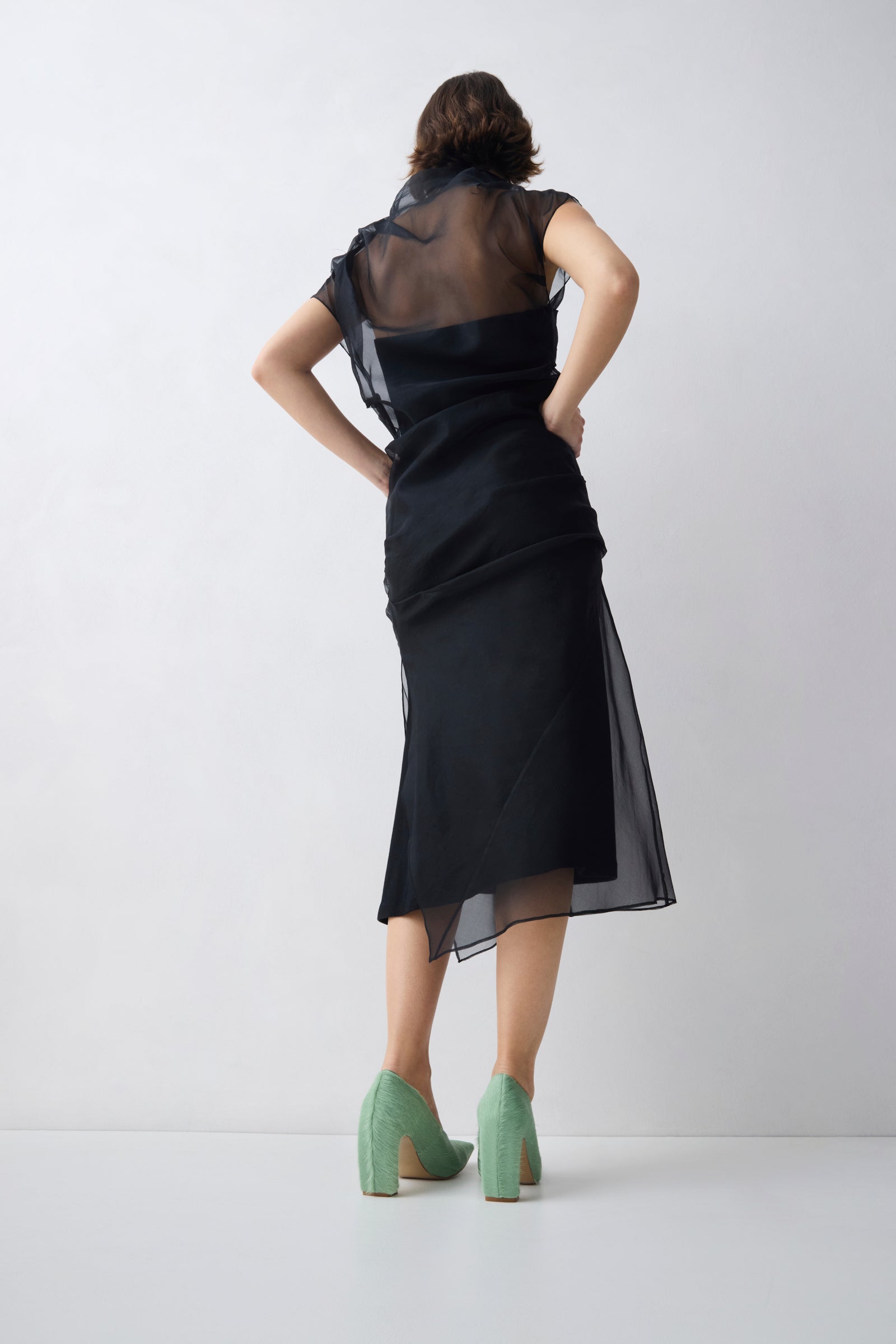 Woman wearing a black dress with sheer sleeves against a white background