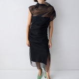Woman wearing a black dress with sheer overlay against a white background
