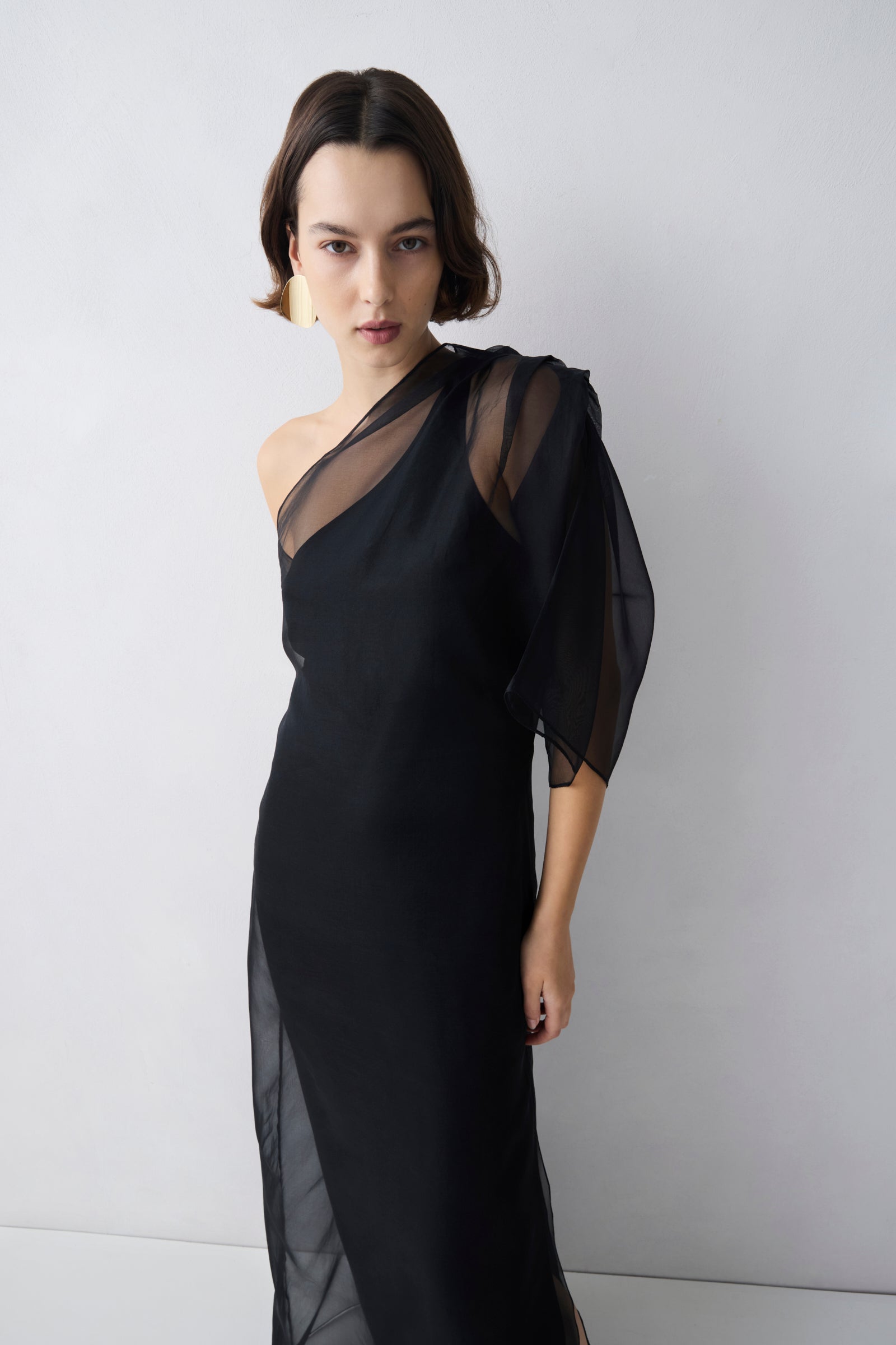 Woman wearing a black one-shoulder dress against a white background