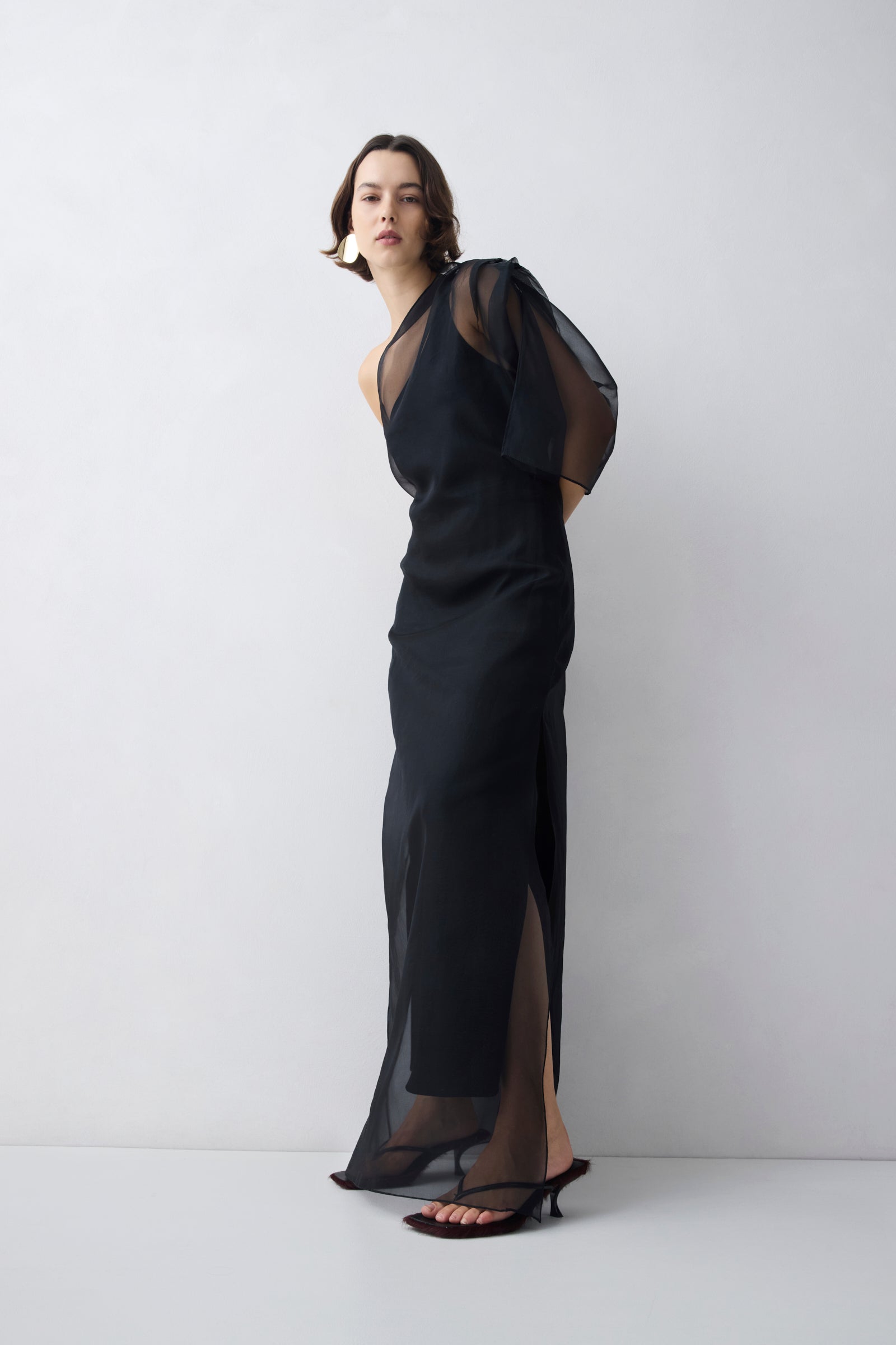 Woman wearing a black evening gown with sheer sleeves against a white background