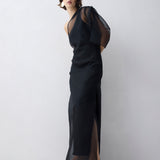 Woman wearing a black evening gown with sheer sleeves against a white background