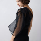 Woman wearing a black dress with sheer sleeves against a white background