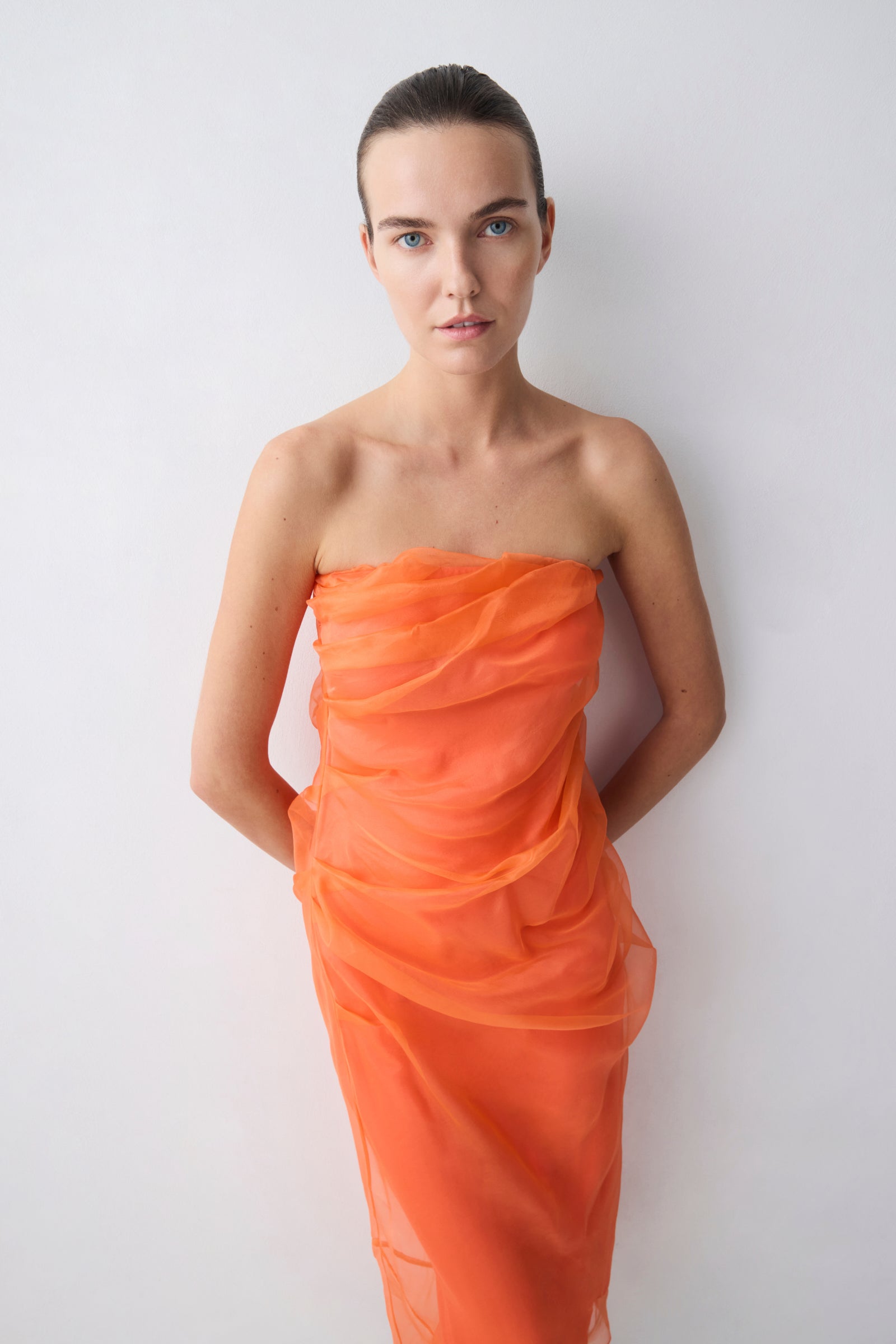 Woman wearing an orange strapless dress against a white background