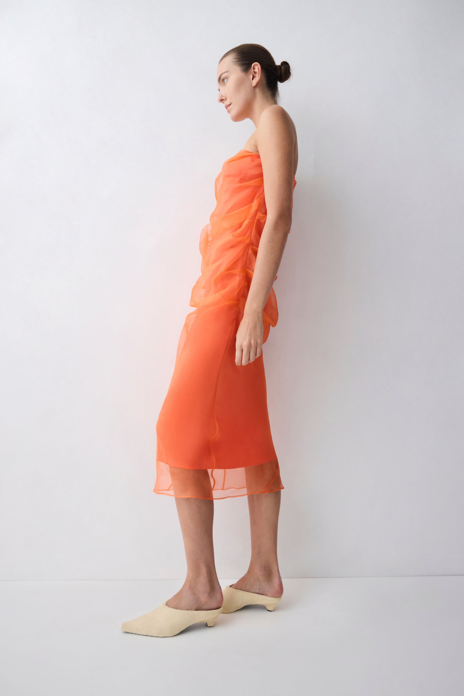 Woman wearing an orange dress standing against a white background