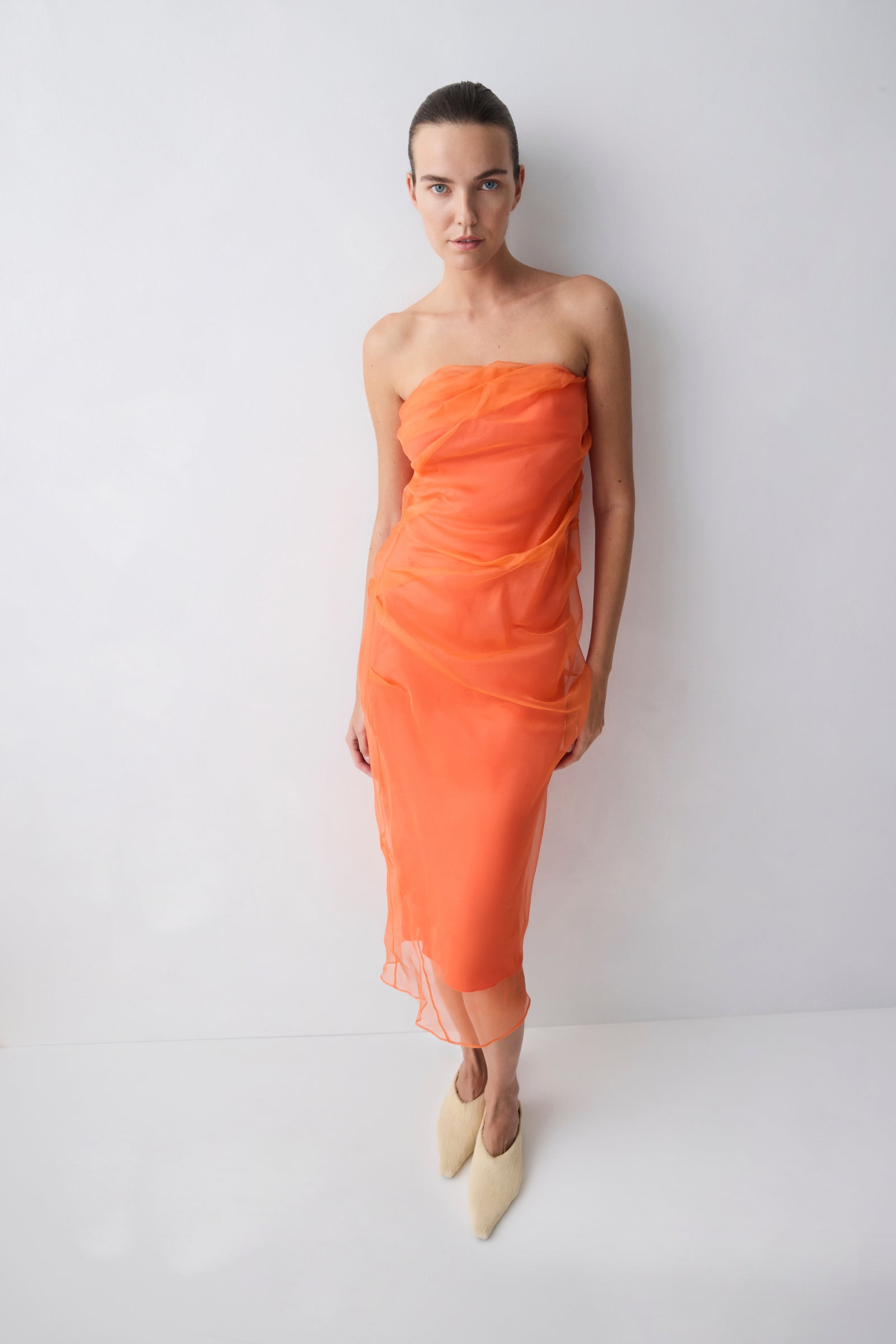 Woman wearing an orange strapless dress against a white background