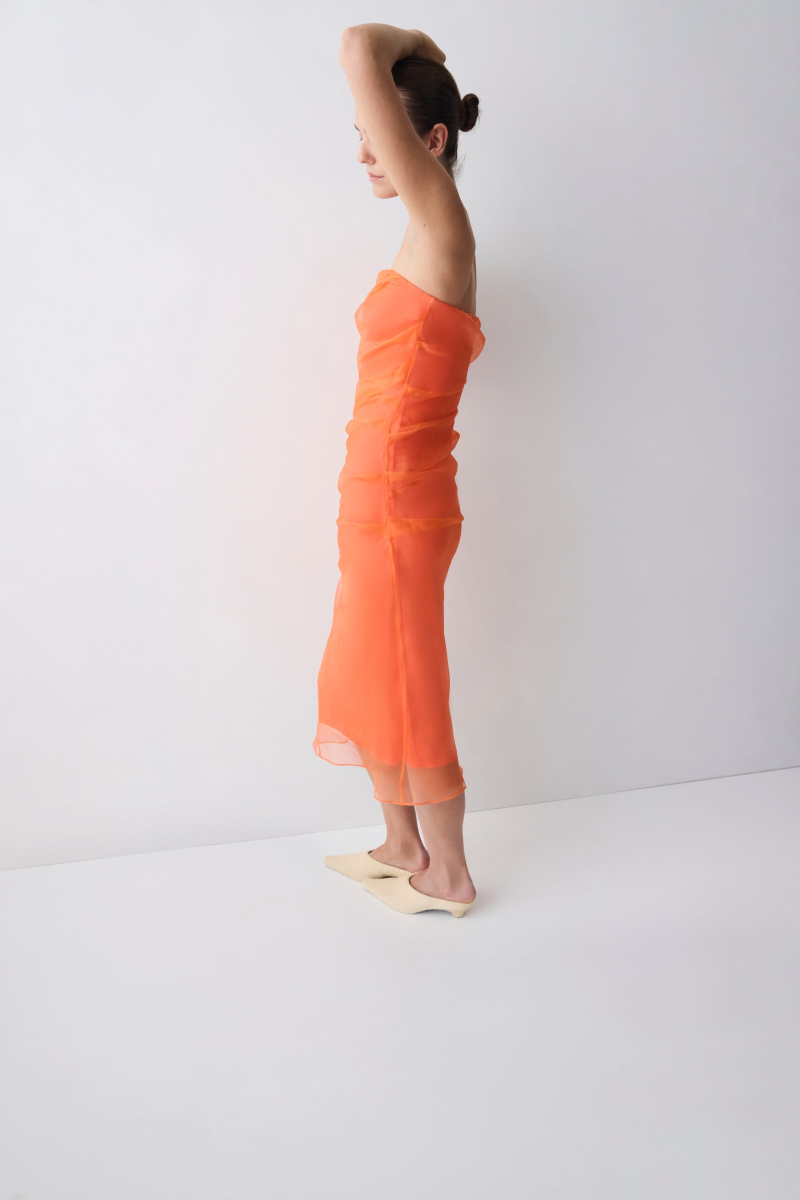 Woman wearing an orange strapless dress against a white background