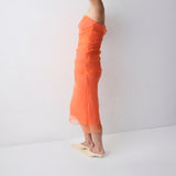 Woman wearing an orange strapless dress against a white background