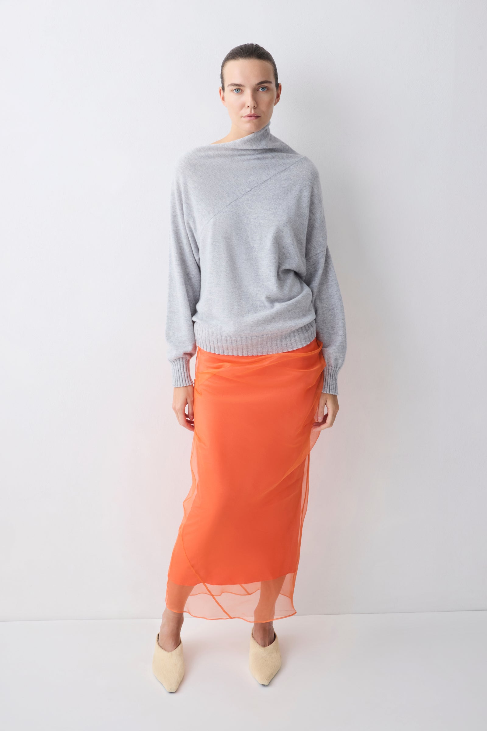 Person wearing a gray sweater and orange skirt on a white background