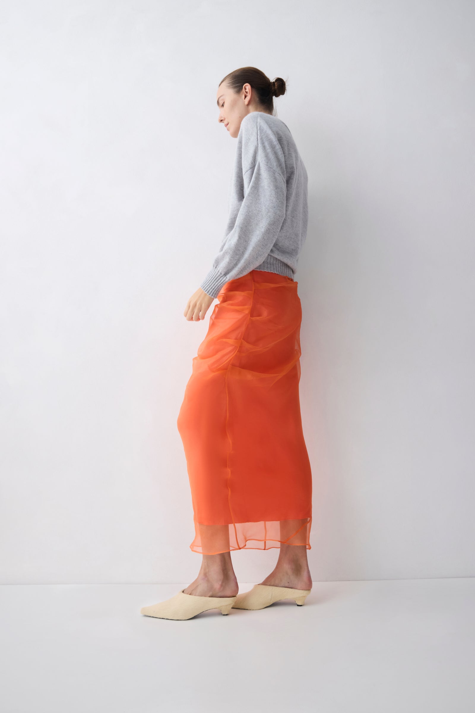 Person wearing an orange skirt and gray sweater against a white background
