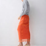 Person wearing an orange skirt and gray sweater against a white background
