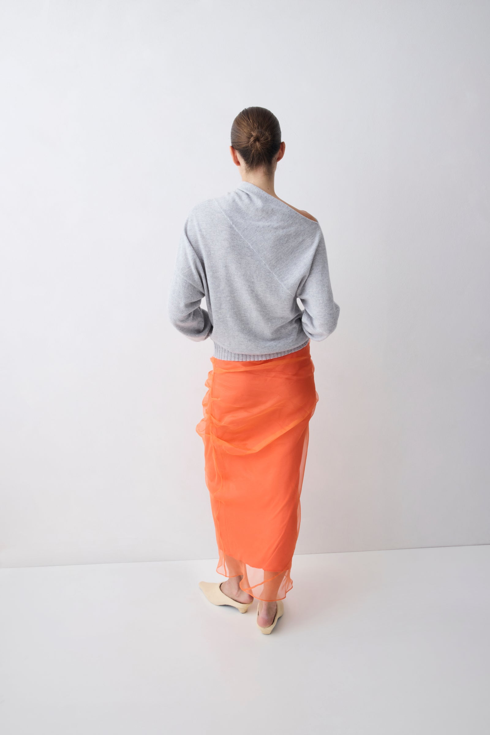 Person wearing a gray sweater and orange skirt on a white background