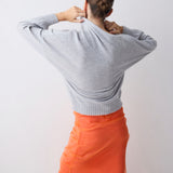 Person wearing a gray sweater and orange skirt against a white background
