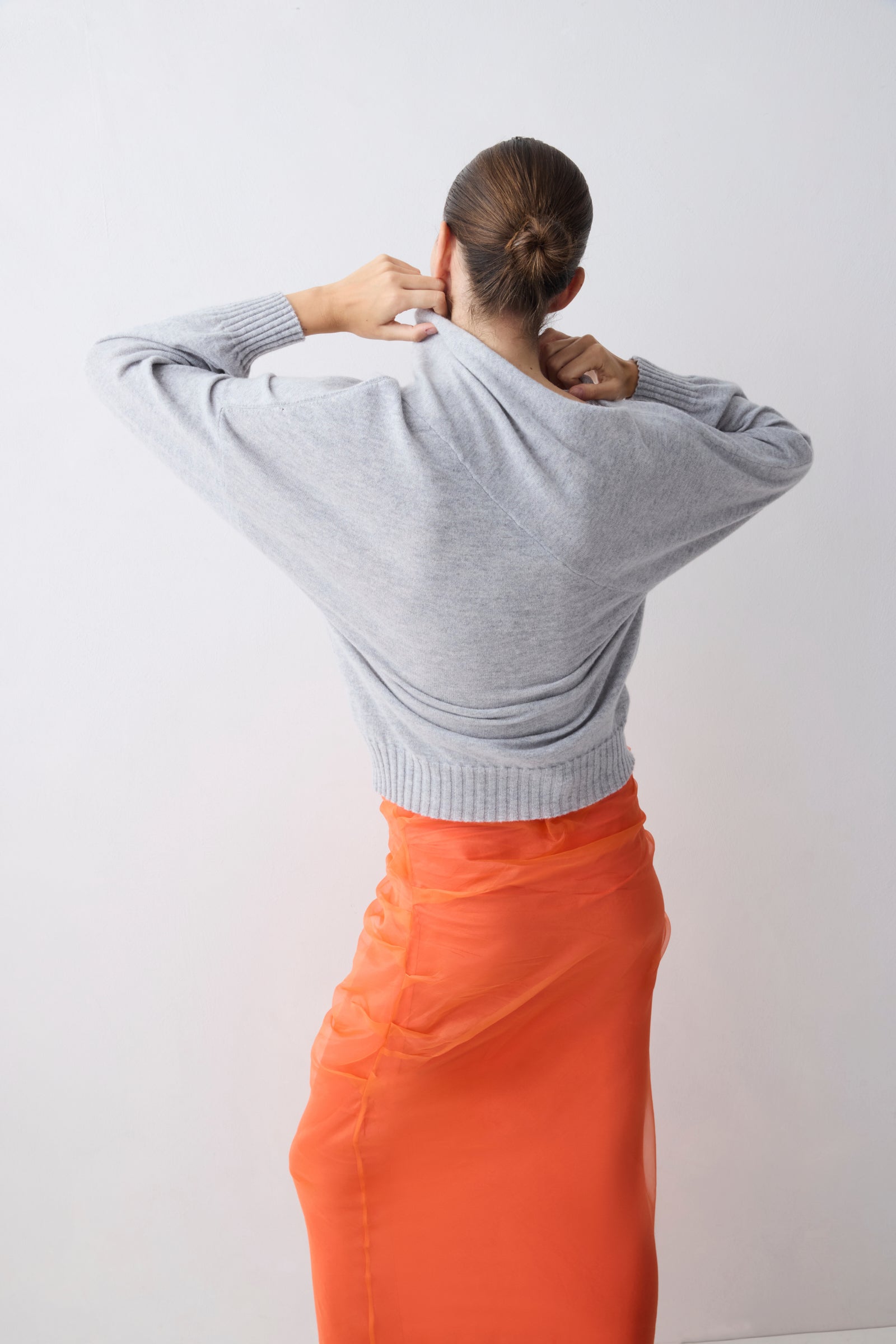 Person wearing a gray sweater and orange skirt against a white background